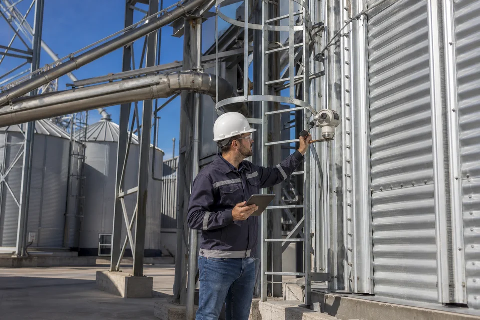 Técnico calibrando instrumentación junto a silos de grano y ductos de transporte
